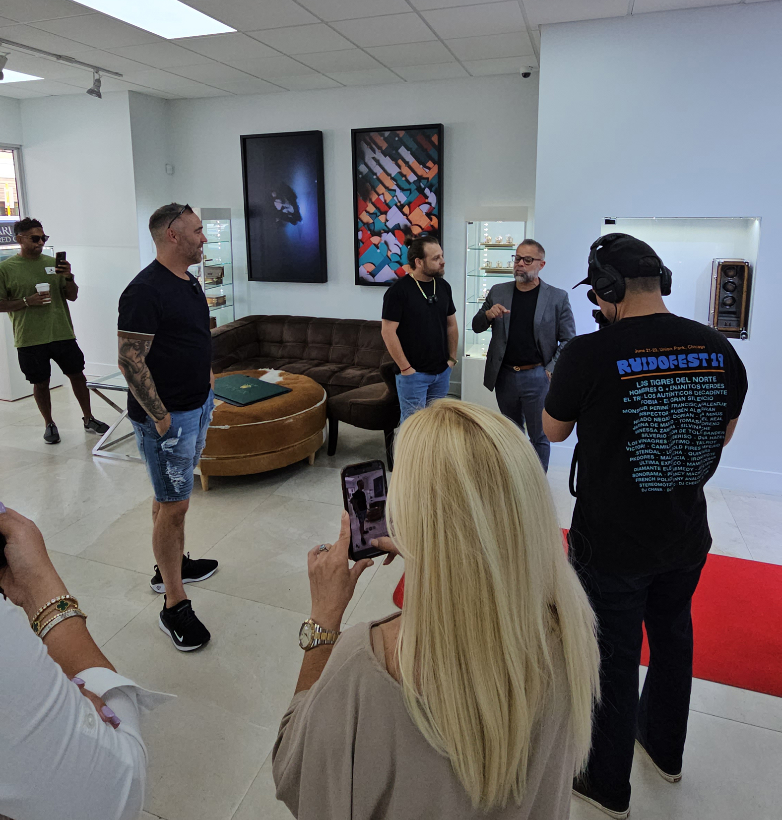 Image of the CRM Jewelers team inside their stylish showroom, creating content for their social media channels. The team is gathered around luxury watches displayed in glass cases, with professional cameras and lighting equipment set up. Some team members are filming product showcases, while others are editing or reviewing footage. The showroom's elegant interior, featuring polished surfaces and upscale decor, reflects the high-end nature of the brand and its content production.